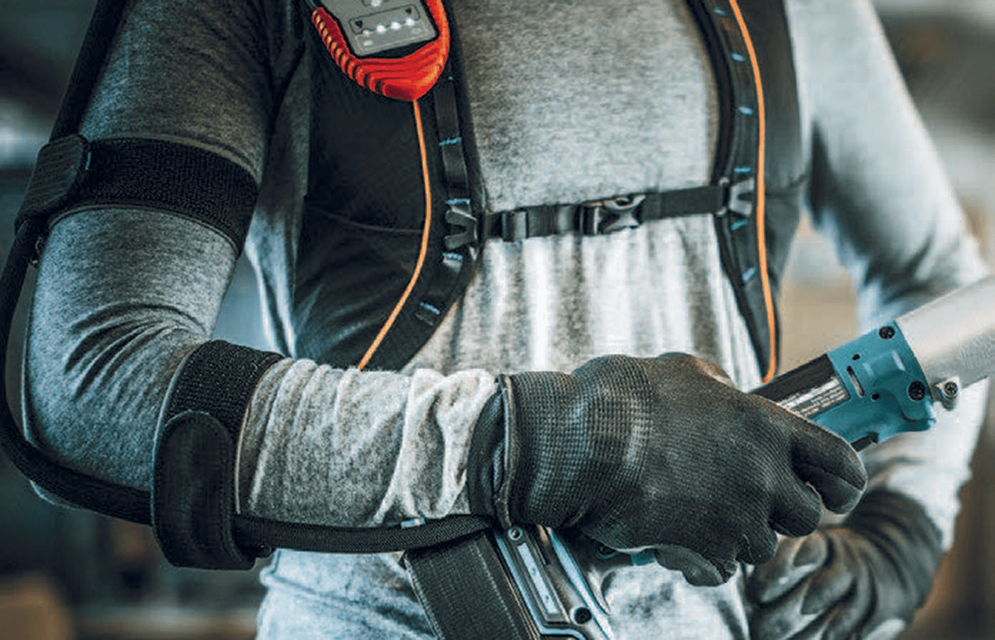 Travailleur équipé d’un exosquelette de soutien des bras utilisant un outil électroportatif.