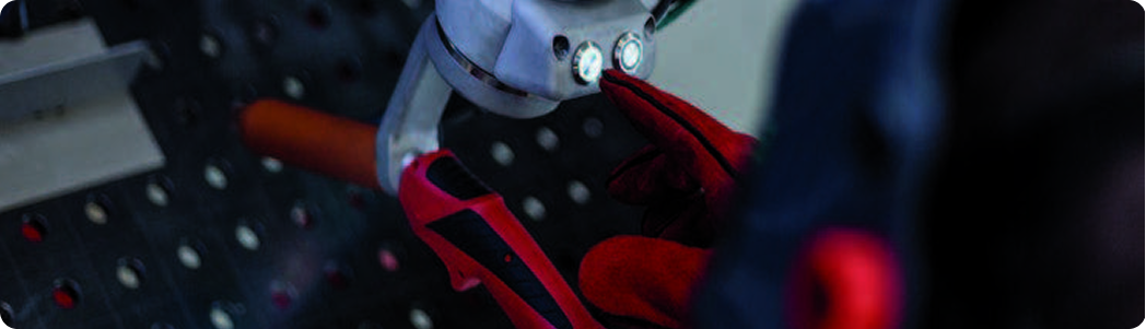 Opérateur ajustant un outil de soudage robotisé sur une table métallique.